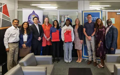 a group photo of school officials with two teenage girls in the middle holding red gift bags. 
