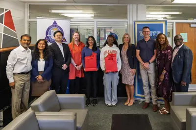 a group photo of school officials with two teenage girls in the middle holding red gift bags. 