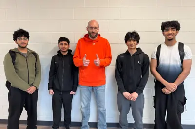 four students posing with a teacher in a school hallway. 