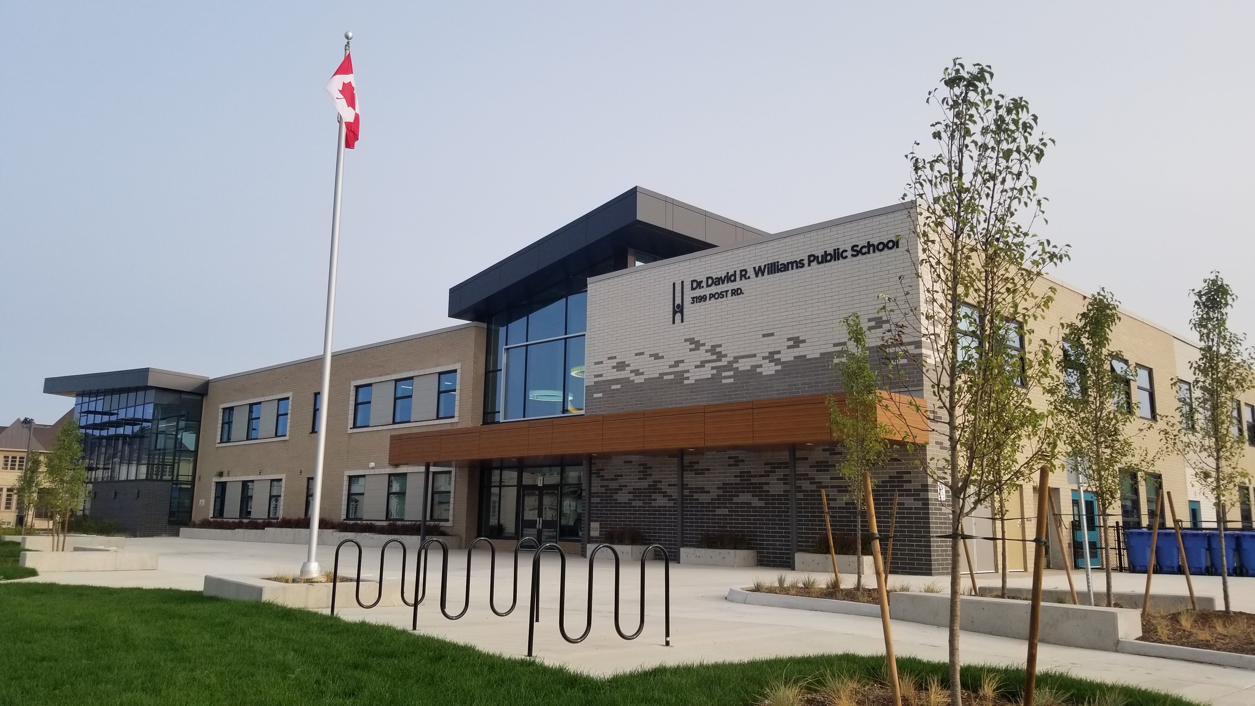 This is an image of the front of the school building including a flag pole, grass, and a bike rack.