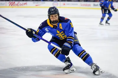 Hockey player in blue uniform skates low to the ice while controlling the puck during a game.