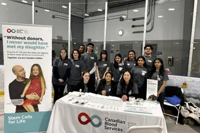 a group of students posing behind a blood donation campaign table. 