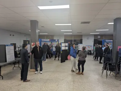 Community members walking through an open information session with multiple stations displaying maps and materials for the Burlington Southwest School Boundary Review