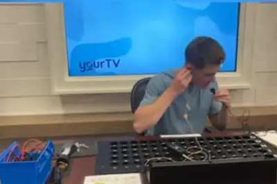 a boy sitting in front of a screen working on a machine while wearing headphones. 