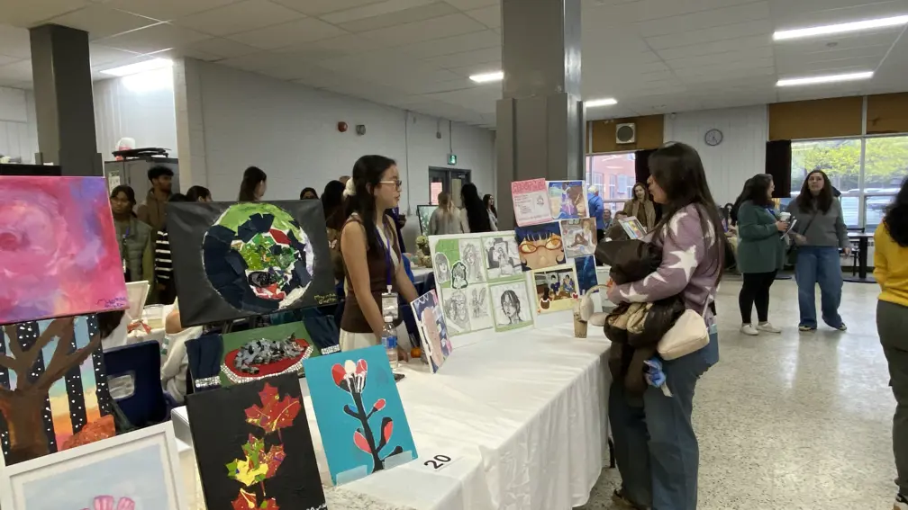 Students and visitors browse artwork displays during a school showcase event in a large indoor hall.