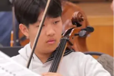 close up of a teenage boys face while playing the cello. 