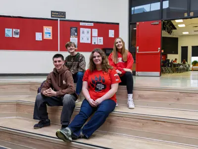 Four students smiling together while seated on steps inside Acton District School.