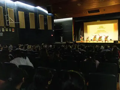 Audience watches student performers on stage during a school showcase event in a theatre auditorium.