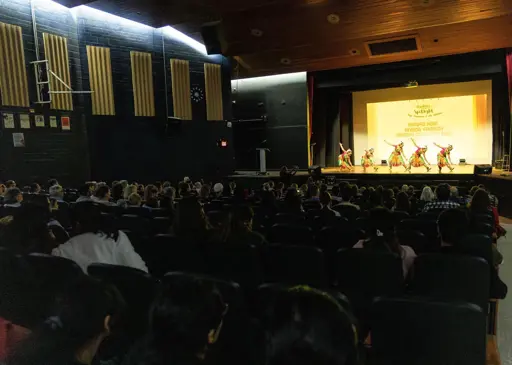 Audience watches student performers on stage during a school showcase event in a theatre auditorium.