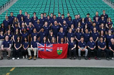a large group of students all wearing navy T-shirts posing with an Ontario flag. 