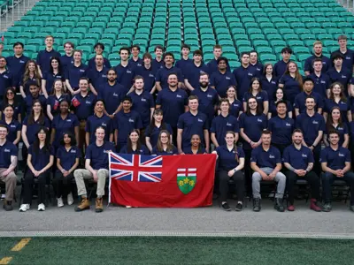 a large group of students all wearing navy T-shirts posing with an Ontario flag. 