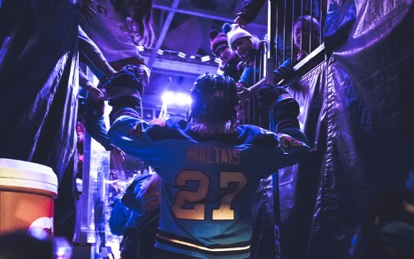 Hockey player wearing jersey number 27 enters the ice through a tunnel, reaching up to high-five fans leaning over the railing.