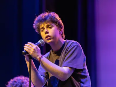 Student performs on stage holding a microphone during a live vocal performance