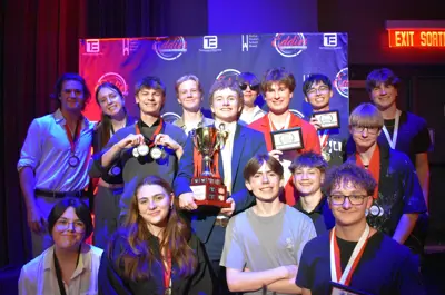 a group of teenagers posing for a picture on stage with the person in the middle holding up the trophy.