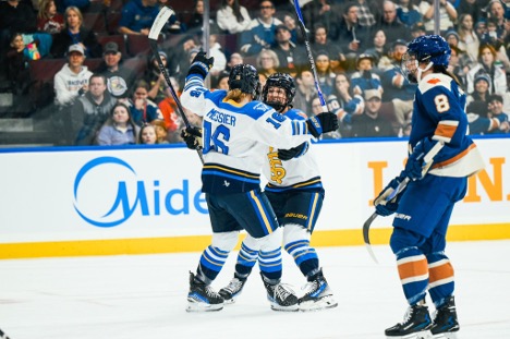 Two hockey players in white jerseys celebrate a goal on the ice as a player from the opposing team skates nearby.