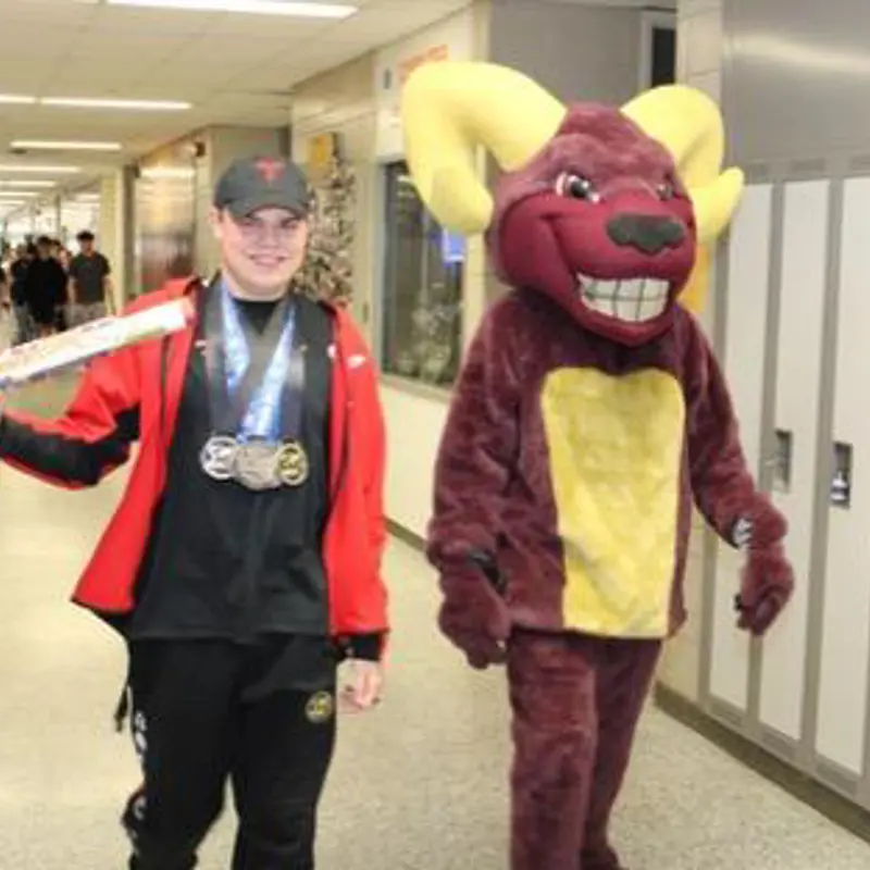 Timothy Billington, wearing his Summer Canada Games medals, leads the King's Baton through the halls of M.M. Robinson High School alongside Robbie the Ram