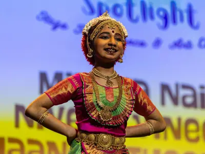 Student performs a traditional dance on stage wearing colourful cultural attire and ornate jewelry during a student showcase event.