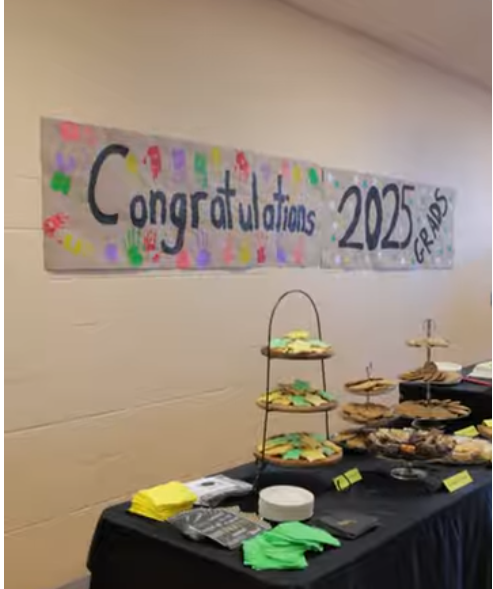 a banner on a school wall that reads "Congratulations 2025 Grads". The banner is placed behind a table that has desserts.