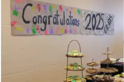 a banner on a school wall that reads "Congratulations 2025 Grads". The banner is placed behind a table that has desserts.
