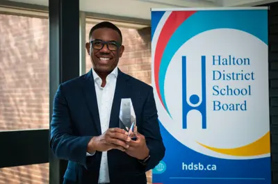 a close up of a man holding up an award in front of a Halton District School Board sign