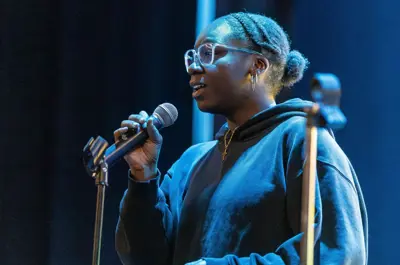 Student speaks into a microphone on stage during a student performance event
