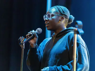 Student speaks into a microphone on stage during a student performance event