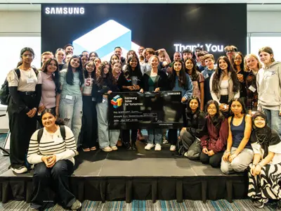 a large group of students posing together, holding a big check in the middle.