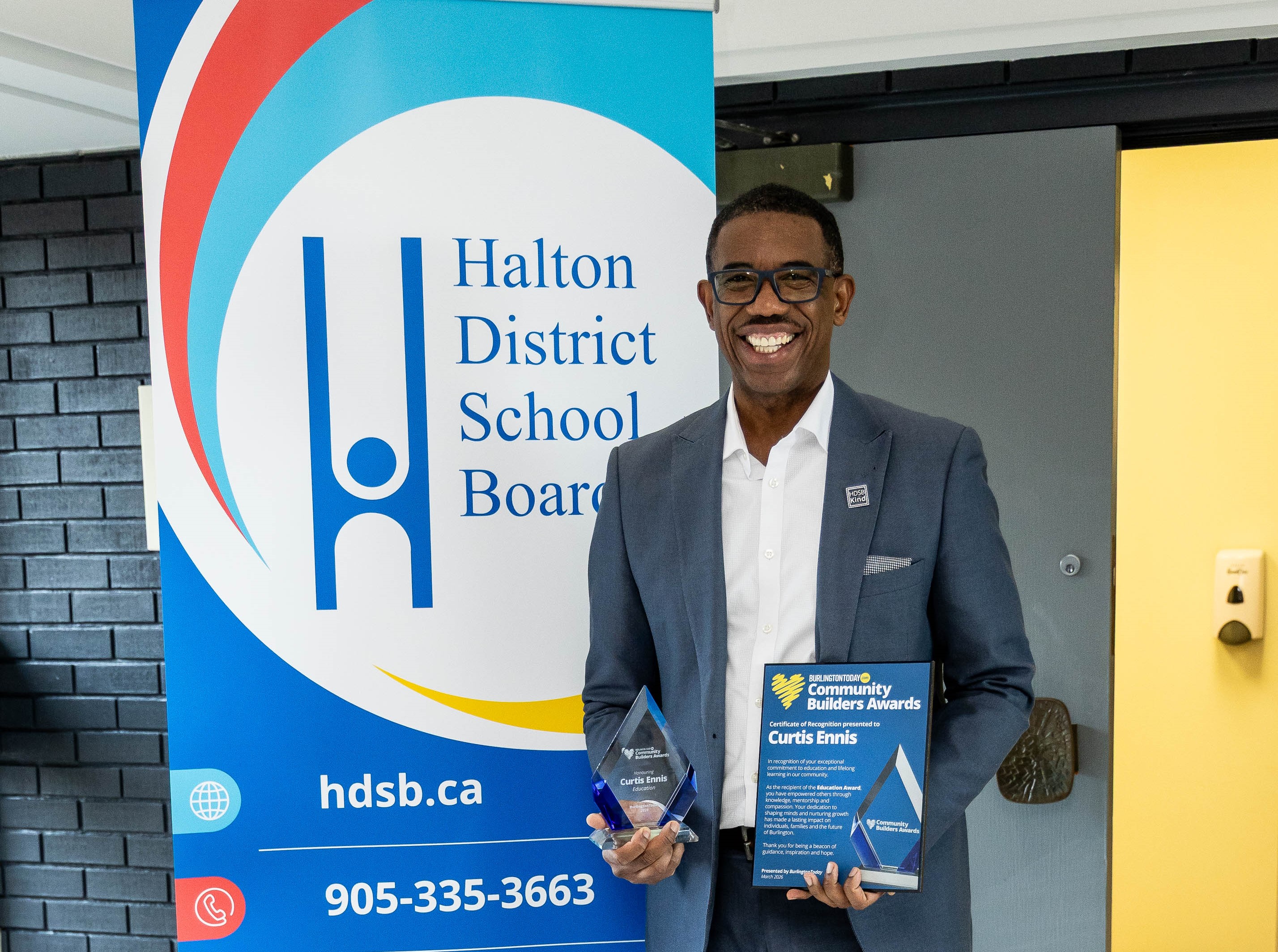 man standing in front of a Halton District School Board banner holding an award in his hand.